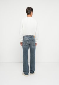 Pull blanc court, jean bleu clair délavé à jambe droite et baskets beiges ; détail subtil de couture sur les poches arrière.