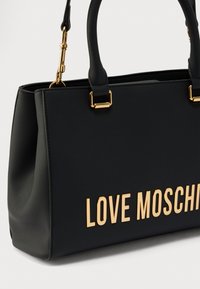 Μαύρη τσάντα χειρός από ψεύτικο δέρμα με χρυσές επιγραφές "LOVE MOSCHINO", δομημένο σχέδιο, διπλές λαβές στην κορυφή και διακοσμητικά στοιχεία στα πλαϊνά.