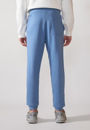 Pantalones de chándal azul claro hechos de tela suave, con un ajuste ajustado, cinturilla elástica y un bolsillo trasero. Con puños acanalados.