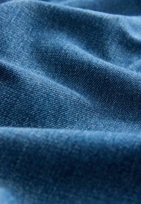 Sinine denimkangas tekstureeritud pinnaga, milles on keskmise raskusega kude ja nähtavad indigo lõngad, mis on paigutatud sujuvatesse, lainelistesse mustritesse.