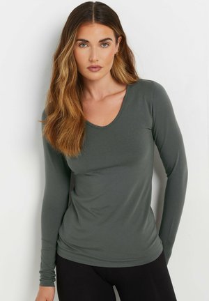 Langärmeliges, olivgrünes V-Ausschnitt-Oberteil aus weichem Stoff, mit tailliertem Schnitt und glatter Textur. Schwarze Leggings runden das Outfit ab.