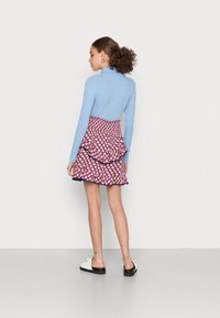Top de manga longa azul claro combinado com uma saia ruffled de padrão multicolorido com formas triangulares e uma cintura fruncida. Calçado branco.