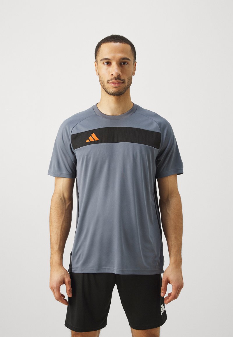 Szary sportowy T-shirt z czarnym paskiem na klatce piersiowej i pomarańczowymi akcentami. Wykonany z lekkiego materiału, z krótkimi rękawami i okrągłym dekoltem.