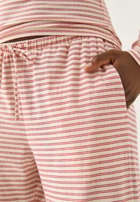 Letterlige pyjamabukser i creme med smalle røde striber, udstyret med elastisk talje med snorelukning og sidelomme.