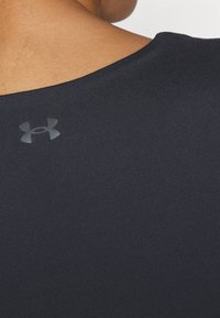 Melna sporta krekla gluda tekstūra. Tam ir apaļš dekoltē un neliels pelēks Under Armour logotips augšējā aizmugurē.