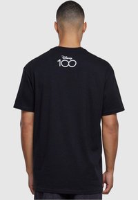 Svart bomull t-skjorte med hvit "Disney 100" logo på ryggen. Klassisk rund hals og korte ermer, med rett snitt.
