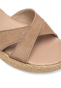 Beige mognutsko s sandalima s križnim trakama, glatkim kožnim uložkom i tkanim jutenim đonom za dodatnu teksturu i izdržljivost.