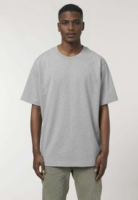 T-shirt oversize grigia in cotone, con maniche corte e scollatura rotonda, indossata da un modello. La texture del tessuto appare liscia.