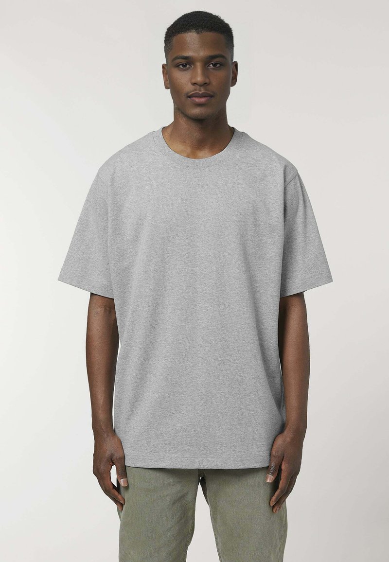 T-shirt oversize grigia in cotone, con maniche corte e scollatura rotonda, indossata da un modello. La texture del tessuto appare liscia.