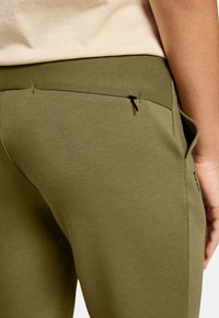 Olivengrønne joggers med en glat tekstur, der har en baglomme med en sort lynlås og en tætsiddende talje.
