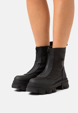 Bottes noires à la cheville avec un dessus texturé, dotées de deux fermetures à glissière à l'avant et d'une semelle en caoutchouc épaisse. Le design combine des matériaux lisses et à motifs.