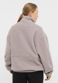 Polarowy pulower w jasnoszarym kolorze z wysokim kołnierzem, luźnym krojem i ściągaczami przy mankietach. Miękka tekstura i detale na szwie ramion.