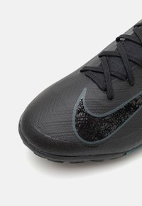 Svart idrottssko med en texturerad yta, med en kontrasterande blank svart Nike-logotyp, svarta snören och en slitstark sula.