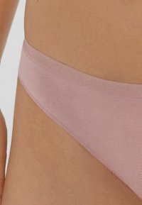 Helle rosa Bikinihose aus glattem Stoff mit einem dünnen, elastischen Bund und nahtlosen Kanten, die ein minimalistisches Design aufweist.