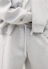 Light gray sweatpants with front drawstring and matching zip-up hoodie partially unzipped over a white shirt.