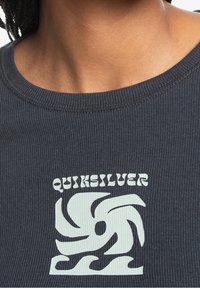 Dunkelgraues, geripptes T-Shirt mit einem weißen Quiksilver-Logo in einem wirbelnden Design. Der Halsausschnitt ist rund und der Stoff hat eine strukturierte Oberfläche.