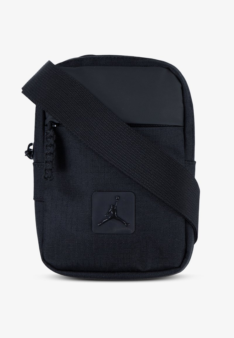 Black fabric sling bag with a textured surface, featuring a zippered pocket, adjustable strap, and a circular logo patch.