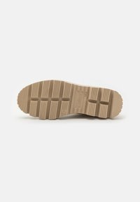 Semelle de chaussure en caoutchouc beige avec texture striée, présentant un motif de bande de roulement bien défini et un marquage. Bords lisses avec un design de bout arrondi.