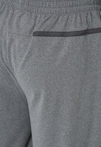 Šedé sportovní kalhoty s texturovanou tkaninou, s elastickým pasem a kapsou s černým lemováním. Volný střih, minimální detaily.