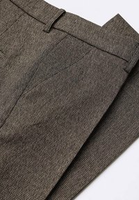 Pantalon en tissu texturé marron foncé, avec une taille plate, des passants de ceinture et des poches latérales. Couture soignée visible sur les coutures.