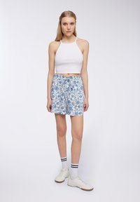 Top in cotone bianco a maniche corte abbinato a pantaloni corti blu con motivo floreale. I pantaloni corti presentano un elastico in vita e una vestibilità ampia e rilassata.
