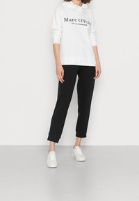 Sudadera blanca con capucha y texto negro, combinada con pantalones de chándal negros ajustados y zapatillas blancas. Tela suave, corte relajado, detalle de cordón.