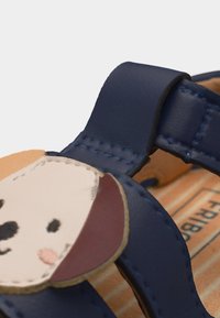 Παιδικό πέδιλο σε ναυτικό μπλε με λεπτομέρεια ραμμένου προσώπου σκύλου στο λουράκι και ριγέ εσωτερική σόλα.