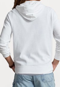 Vit hoodie i mjukt tyg med dragsko i huvan, ribbade ärmslut och midja, bärs över ljusblå cargo-byxor.