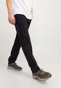 Černé slim fit džíny mají klasický pětikapsový design, doplněné šedými teniskami s texturovanými akcenty a polstrovanou podrážkou.