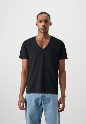 Schwarzes V-Ausschnitt-T-Shirt aus weichem Stoff, mit kurzen Ärmeln und lässiger Passform, kombiniert mit hellblauen Jeans.