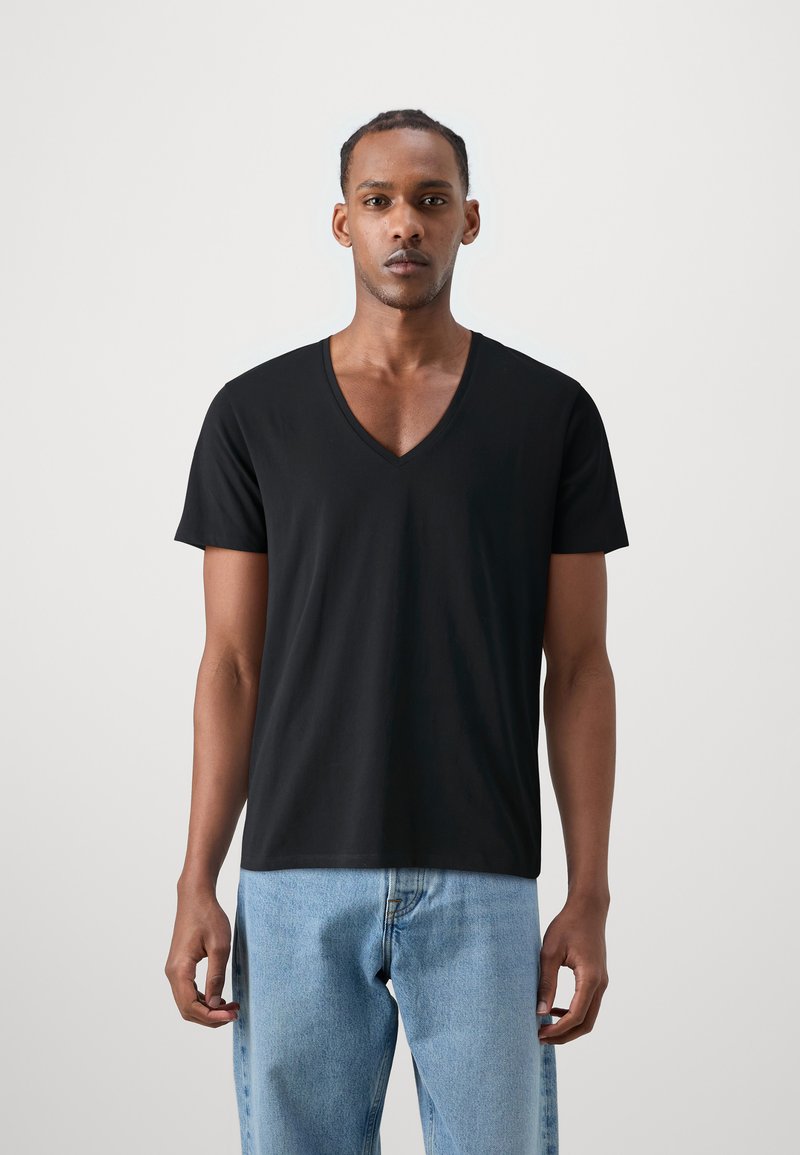 Tricou negru cu guler în V, realizat dintr-un material moale, având mâneci scurte și o croială lejeră, asortat cu blugi din denim de un albastru deschis.
