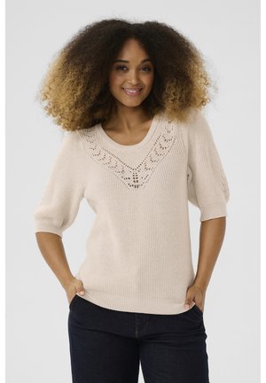 Cream knit sweater with a wide neckline and short puff sleeves, featuring a textured pattern around the front yoke. Dark jeans complement the look.