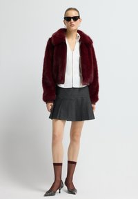 Burgundská bunda z umělé kožešiny s límcem, bílá blůza na zip, tmavě šedá skládaná sukně, vínové ponožky a stříbrné lodičky na vysokém podpatku.