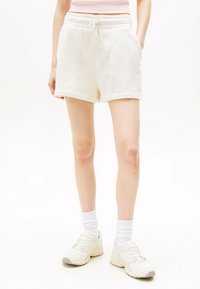 Pantalones cortos de algodón color beige claro con cinturilla elástica, cordón y bolsillos laterales. Presentan una textura suave y un diseño casual.