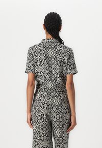 Combinaison à manches courtes noir et blanc à motif, avec un col, présentant un motif en losanges et une taille cintrée.