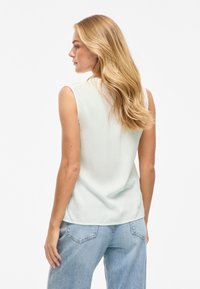 Top sin mangas de color verde claro en una tela suave, combinado con jeans de mezclilla azul claro de tiro alto con un diseño clásico de cinco bolsillos.