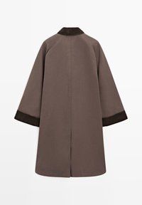 Lungo cappotto marrone con colletto scuro texturizzato, maniche ampie e taglio dritto. Il tessuto appare liscio, con polsini a contrasto.