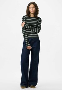 Svītrains garām piedurknēm tops tumši zaļā un krēmkrāsā, pārī ar platām kājām tumšā džinsa biksēm. Mīksta tekstūra un pieguļošs dizains ar ribotu adījumu.