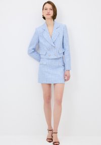 Vaaleansininen tweed-bleiseri, jossa on lyhyt malli ja kaksiriviset napit, yhdistettynä sopivaan minihameeseen. Tasainen pinta, ei kuvioita.