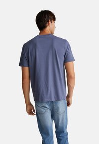 Camiseta de manga corta y cuello redondo en algodón azul apagado. Presenta un corte relajado y una textura suave. Combinada con jeans de denim azul claro.