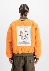 Reversible bomber jacket in orange with ribbed green collar and cuffs. Features a large graphic patch on the back with text and illustrations.