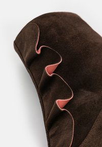 Brązowy zamszowy obiekt z falbaniastym brzegiem z różowym akcentem. Tekstura jest miękka, a design gładki, akcentując kontrastujące kolory.