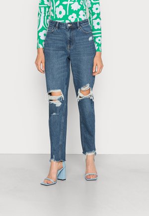 Jeans de denim azul desgastados com grandes rasgos nos joelhos e bainhas desfiadas, combinados com sandálias de salto bloco azul claro.