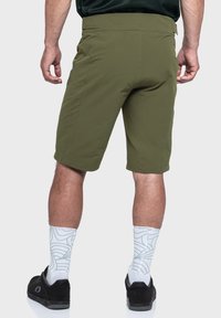 Olivgrüne Shorts aus leichtem Material mit flachem Bund, Gesäßtaschen und kombiniert mit gemusterten weißen Socken und schwarzen Schuhen.