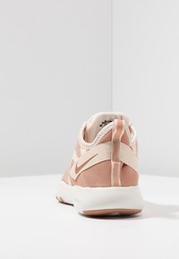 Nike sneakers met een lichtroze mesh bovenwerk, witte zool en een beige accentriem. De achterkant heeft een gladde textuur en logodetail.