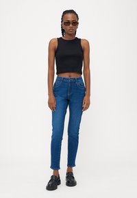 Črna skrajšana majica na naramnice, v kombinaciji z modrimi ozkimi denim hlačami, ki imajo sprednje žepe in gumbasto zapiranje, dopolnitev s črnimi loafer čevlji.