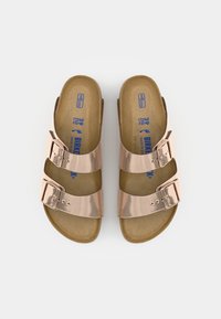 Rose gold sandals with two adjustable metallic straps, cork footbed, and a brown outsole. Designed for comfort and easy wear.