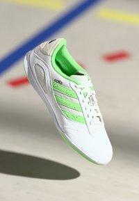 Scarpa da ginnastica bianca con accenti verde, tomaia in rete, tre strisce e una suola testurizzata. Design leggero adatto per sport e abbigliamento casual.