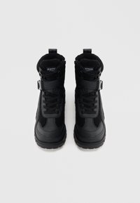 Fekete téli csizma texturált felsőrésszel, műszőrme díszítéssel, fűzős és pántos záródással, valamint vastag talppal a jó tapadás érdekében.