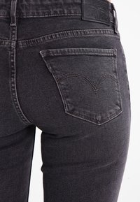 Vaqueros de mezclilla negra con un diseño ajustado, que cuentan con un bolsillo trasero con una costura curva distintiva y una etiqueta de cuero en la cintura.